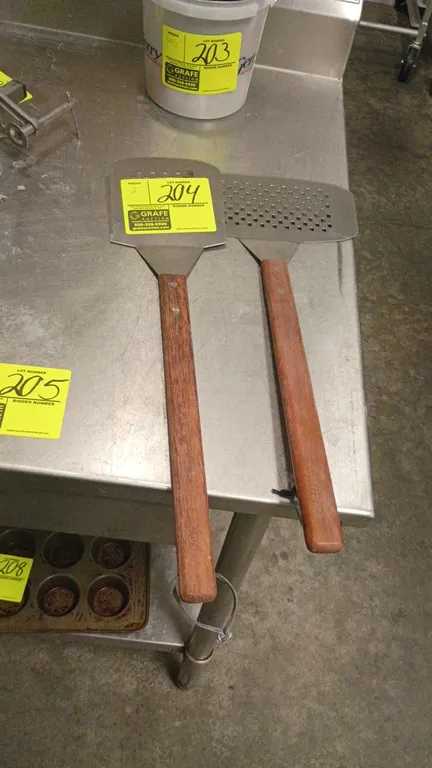Stainless steel grill spatulas. Features perforated turners, one with a serrated cutting edge, and long riveted wood handles with hanging loops.