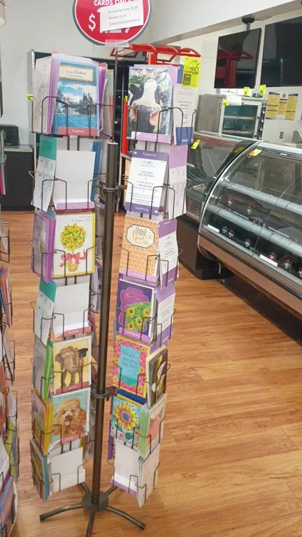 Rotating greeting card display rack. Features multi-tier wire card pockets, top sign holder, and assorted greeting card inventory. 22" x 78". Mounted