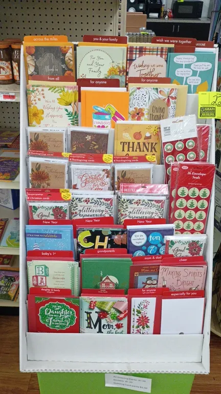Corrugated cardboard greeting card floor display unit. Features multi-tier shelving design. Includes assorted greeting cards, card packs, and envelope