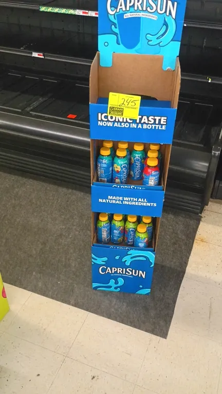 Capri Sun corrugated cardboard retail bottle display stand. Features multi-tier shelving with branded point-of-purchase graphics and assorted Capri Su