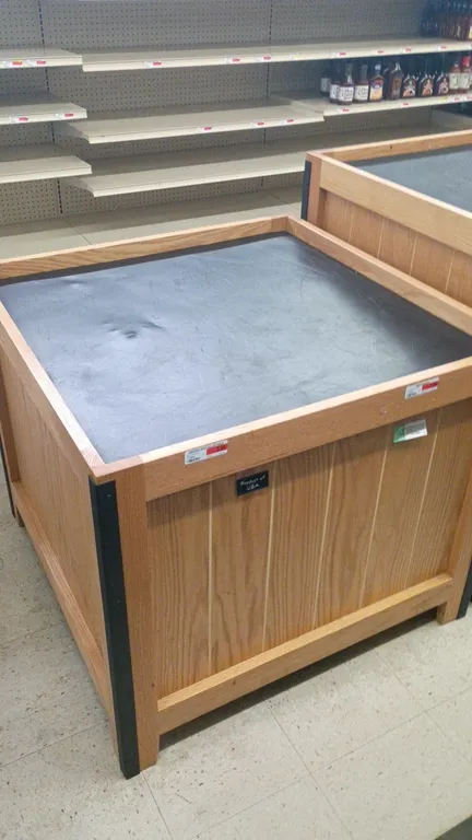 Wooden produce dump tables. Features wood-finish paneled construction, black corner bumper trim, and raised perimeter edges with recessed display tops