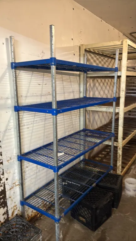 4-tier metal wire shelving rack. Features 4 blue coated wire shelves and galvanized metal upright posts. Dimensions: 4' x 6'. Crates and background it
