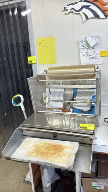 2-roll film wrapping station. Features 2-roll capacity, stainless steel wrapping shelf, heated seal plate, and cut-off bar. Scale and surrounding cont