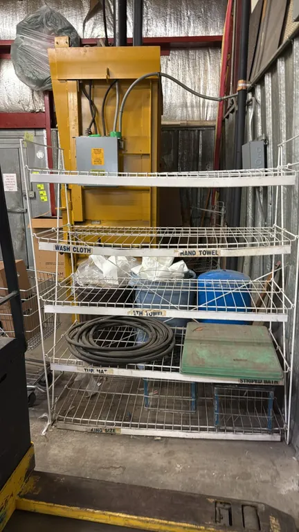 Metal merchandise display rack. Features 5 tiered wire shelves with label channels. Includes coiled black hose, folding table top, and wire baskets. 5