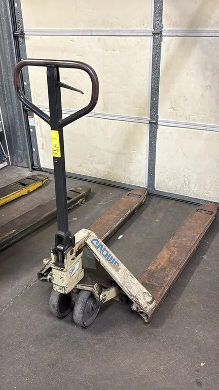 Crown manual pallet jack. Features a loop handle with fingertip release lever, hydraulic lift pump mechanism, dual steer wheels, and load wheels.
