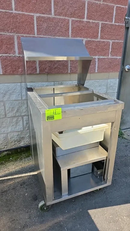 Stainless steel portable breading station. Features an overhead hood, open well top with divider, interior stainless shelf, and plastic tub. 24" x 30"