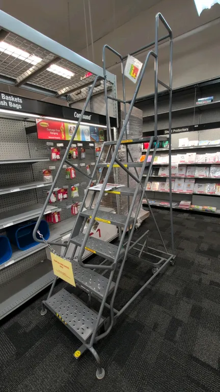 Rolling metal stock ladder. Features 7-step design with perforated steel slip-resistant treads, safety handrails, and upper platform guardrails. Dimen
