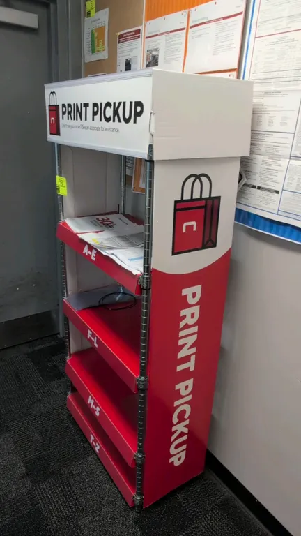 Metal 5-tier print pickup display rack. Features chrome wire uprights, red shelving tiers with alphabetical section labeling (A-E, F-L, M-S, T-Z), and