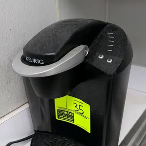 Keurig single-serve coffee maker. Features K-Cup pod brewing chamber, side water reservoir, push-button brew size selection, and removable drip tray.