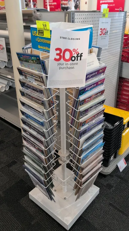Metal rotating merchandise display rack. Features 4-sided wire tiered pockets and top header display. 58"H. Mounted on a square base. Contents not inc