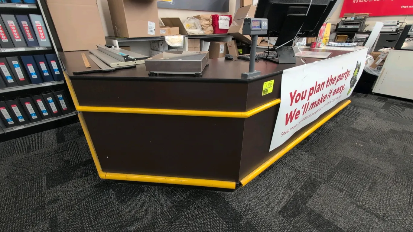 Laminate L-shaped service counter. Features under-counter open shelf storage, single utility drawer, and yellow exterior bumper rails. 9' x 10'. Conte