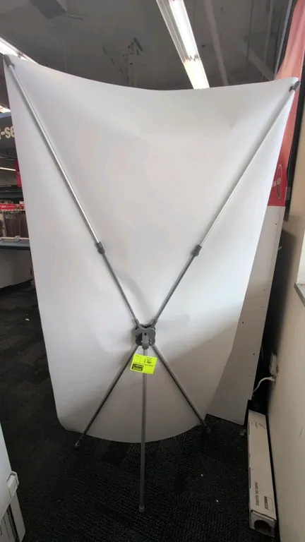 Metal X-frame banner sign stand. Features collapsible tension support arms with central hub and rear tripod support leg. Includes attached blank white