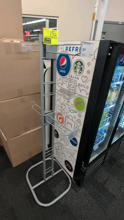Metal merchandise display rack. Features dual-sided hanging display arms with integrated label holders and ladder-style upright frame. 57"H. Mounted o