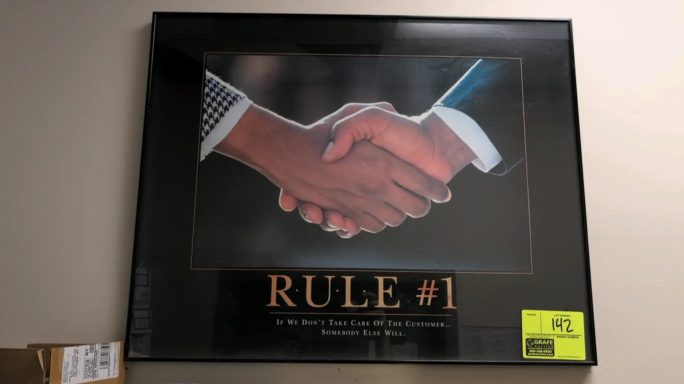 Framed motivational poster titled "Rule #1: If We Don't Take Care Of The Customer... Somebody Else Will." Features a handshake photograph mounted in a