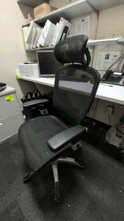 Ergonomic mesh office chair. Features black mesh seat, high mesh back, adjustable headrest, lumbar support, and adjustable armrests. Mounted on a silv
