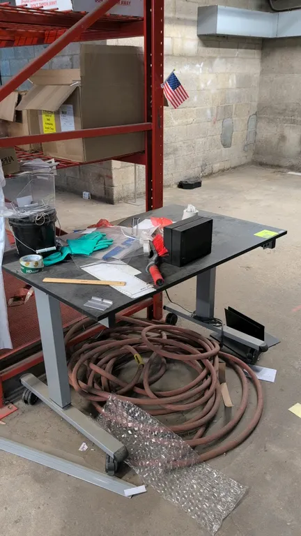 Electric sit-stand portable desk. Features a black laminate top and push-button height adjustment controls. 4'L. Mounted on a gray metal base with cas