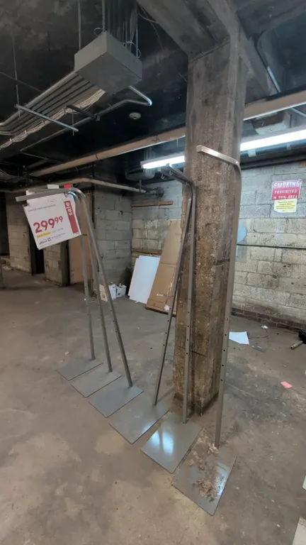Metal adjustable sign stands. Features telescoping adjustable-height uprights, overhead hanging arms with hooks, and flat metal base plates.