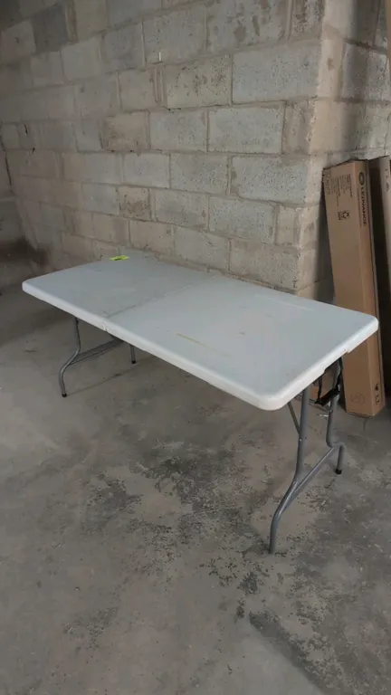 Poly fold-in-half table. Features molded plastic top, integrated carry handle, built-in transport wheels, and folding metal legs. 60"L.