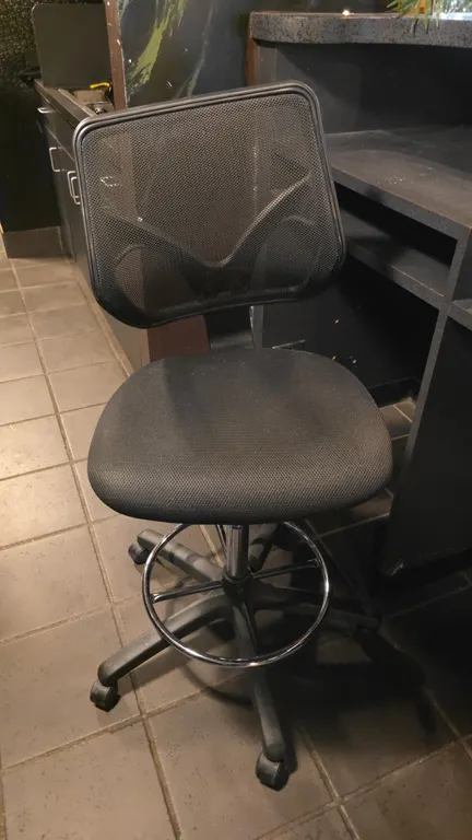 Adjustable drafting chair and metal bar stool. Drafting chair features a black mesh back, upholstered cushioned seat, pneumatic height adjustment, int