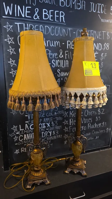 Vintage metal table lamps. Features ornate cast pedestal bases with decorative urn accents and fabric bell shades with tassel fringe trim.