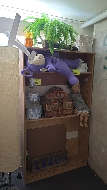 Assorted decorative and novelty items. Includes faux tiered display cake, carved wooden house-style chest, plush Teletubby, articulated doll, painted