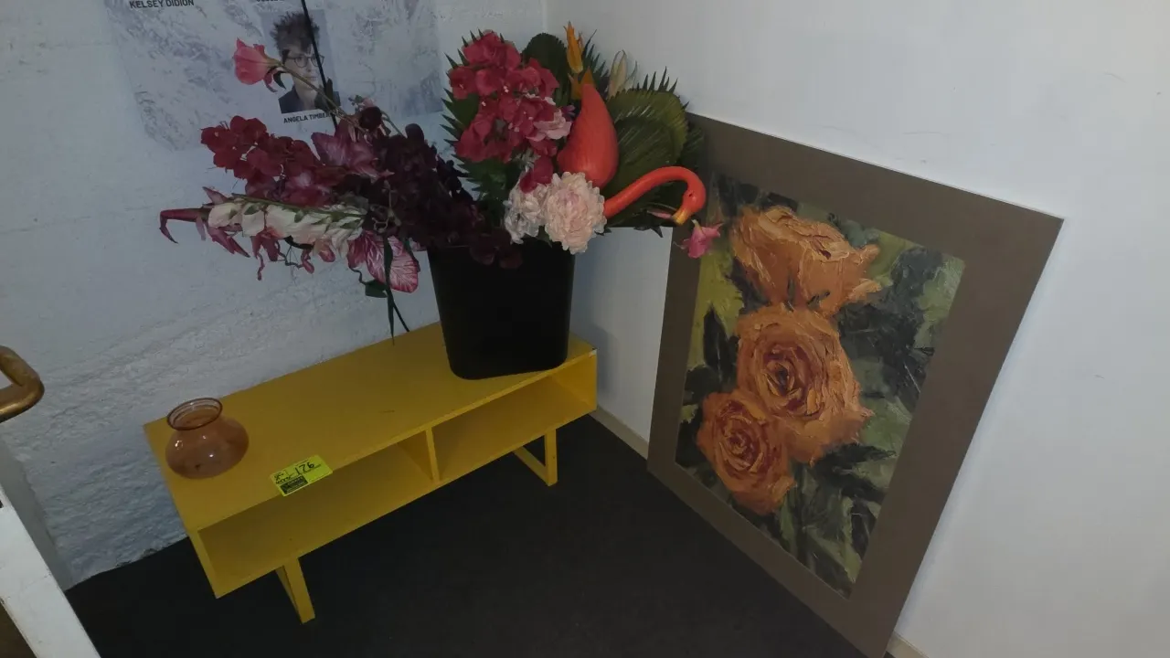 Yellow low console table with 2 open cubbies. Includes amber glass vase, faux floral arrangement in black container with flamingo accent, and matted r