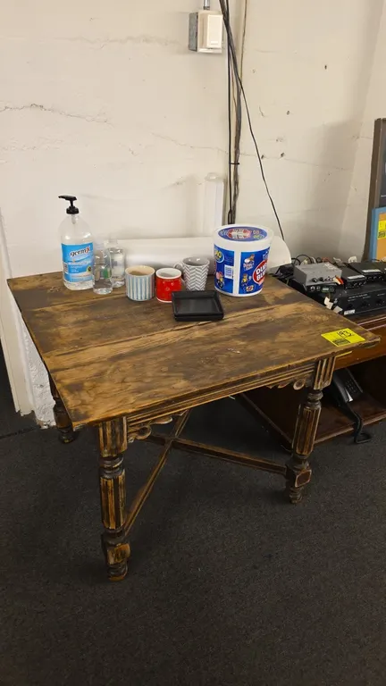 Wood table with tabletop contents. Features rustic plank-style top, turned legs with carved apron details, and an X-stretcher base. Includes assorted