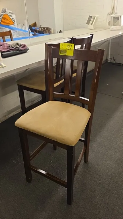 Cushioned wood bar height chairs. Features dark wood frame construction, vertical slat-back design, tan upholstered cushioned seats, and integrated fo