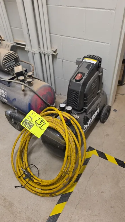 Husky 8-gallon portable air compressor. Features dual pressure gauges, quick-connect fitting, integrated handle, and included yellow air hose. Specifi