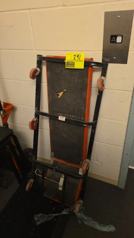 Team Mechanix mechanics creeper. Features orange vinyl padded cushion and metal frame. 40"L. Mounted on swivel casters. Note: Underside backing is tor