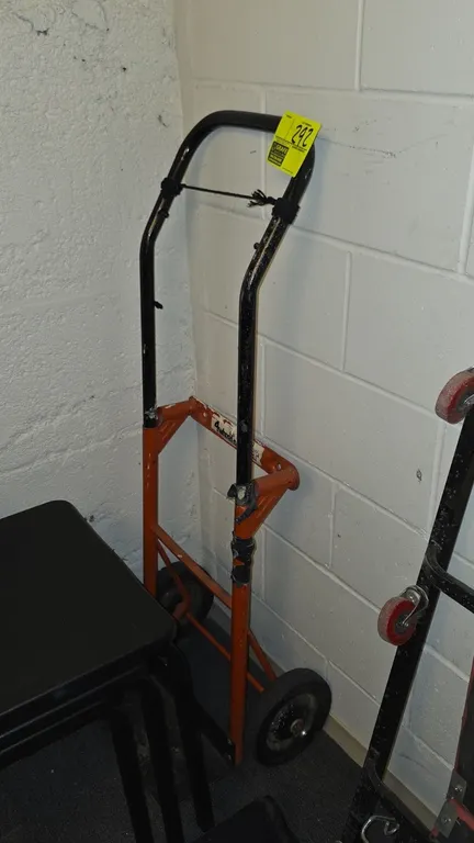Metal hand truck. Features a tubular steel frame, top loop handle, and two solid wheels. Note: Frame shows taped repairs.