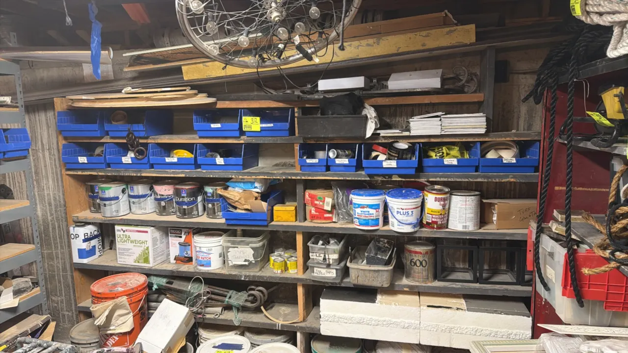 Assortment of tapes, roof coating, paints, adhesives, and maintenance supplies on a multi-tier wood shelving unit. Includes various specialty and util