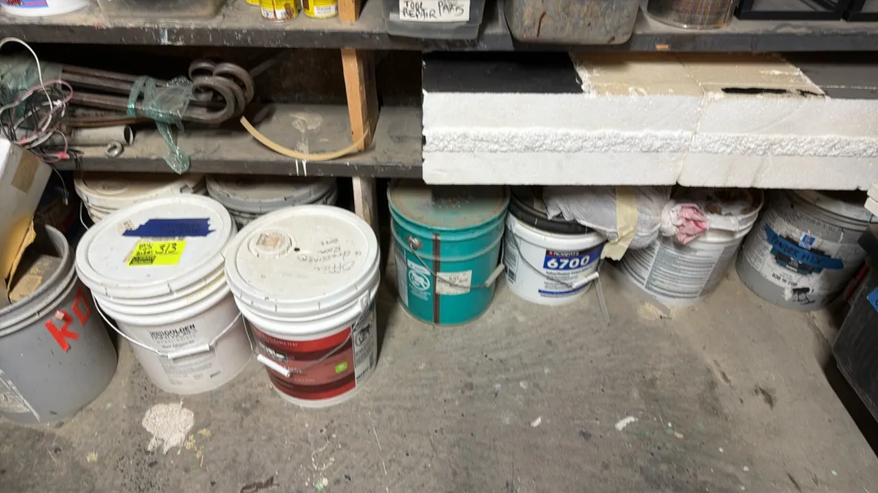 Assorted paints and adhesives lot. Includes various 5-gallon buckets containing paints, coatings, and adhesives from brands including Roberts, Behr, a