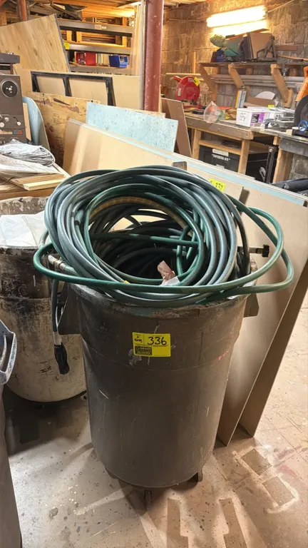 Poly utility trash can with assorted garden hoses. Includes coiled garden hoses with fittings and spray nozzle. Mounted on a rolling dolly base with c
