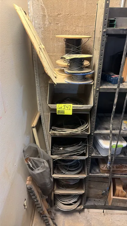 Assorted cables and metal storage organizer. Includes assorted spools and coiled lengths of cable and wire rope housed in a multi-tier vertical metal