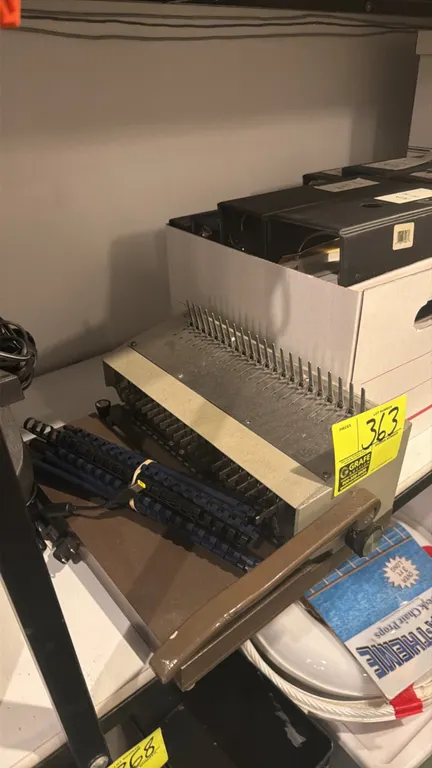Manual tabletop comb binding machine. Features metal construction, side-lever operation, and comb spreader fingers. Includes assorted plastic binding