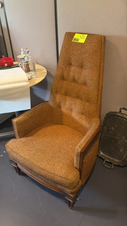 High-back upholstered lounge chair. Features button-tufted tall backrest, textured woven cloth upholstery, and wood trim with tapered legs.