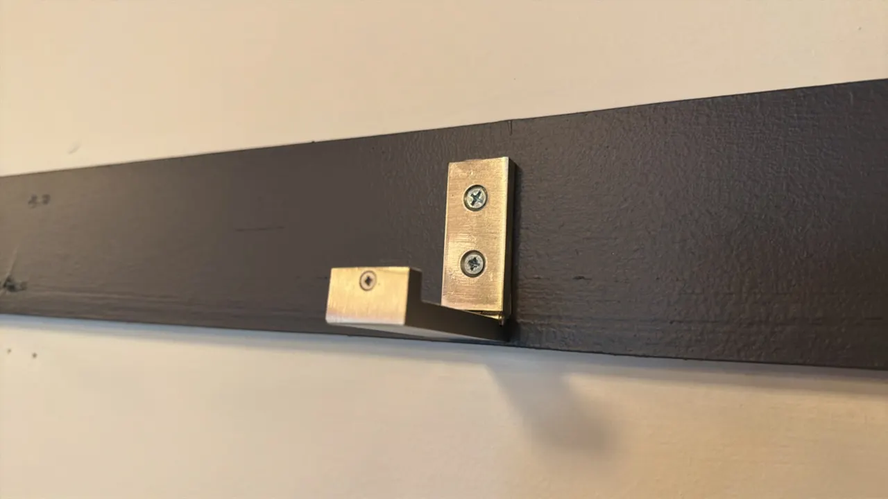 Wall-mounted coat rack. Features (16) flip-down metal hooks mounted on a painted wooden rail.