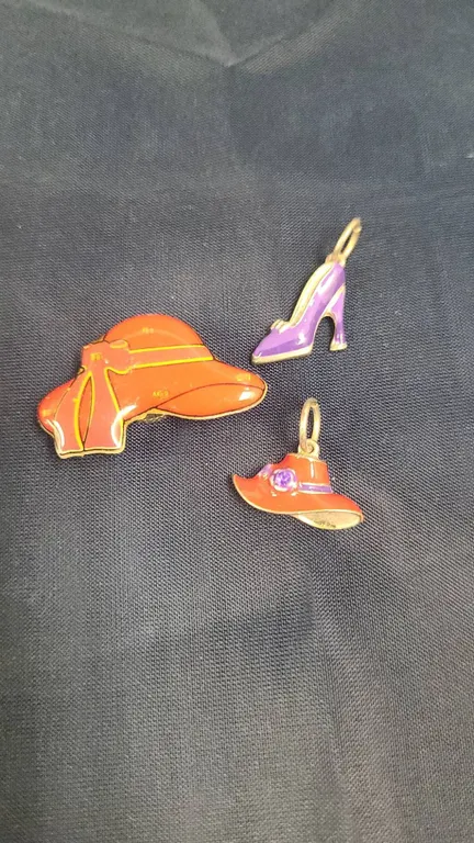 Three Enamel and Metal Accessories: Red Hat Brooch, Red Hat Charm, and Purple High Heel Charm