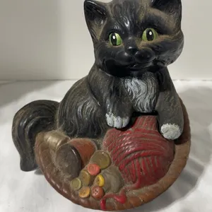 Ceramic cat balled up in a basket of yarn and buttons