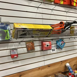 NEW/UNUSED ITEMS ON WALL BETWEEN THE ORANGE RIBBONS - 2 - CAULKING GUNS, MAGNETIC TAPE, SCREW STUDS, 2 - ROLLS OF 3/4" GALVANIZED 24 GAUGE STRAPPING &
