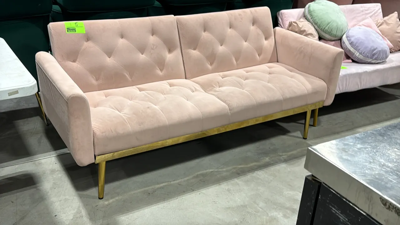 Upholstered loveseat. Features light pink tufted fabric upholstery, split-back design, and gold-tone metal base trim. 69"L. Mounted on tapered gold-to