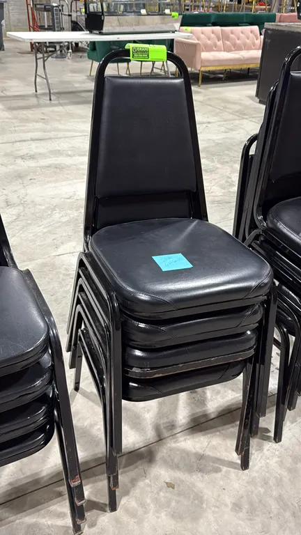 Stackable banquet chair. Features black vinyl upholstered padded seat and backrest with a black metal frame.
