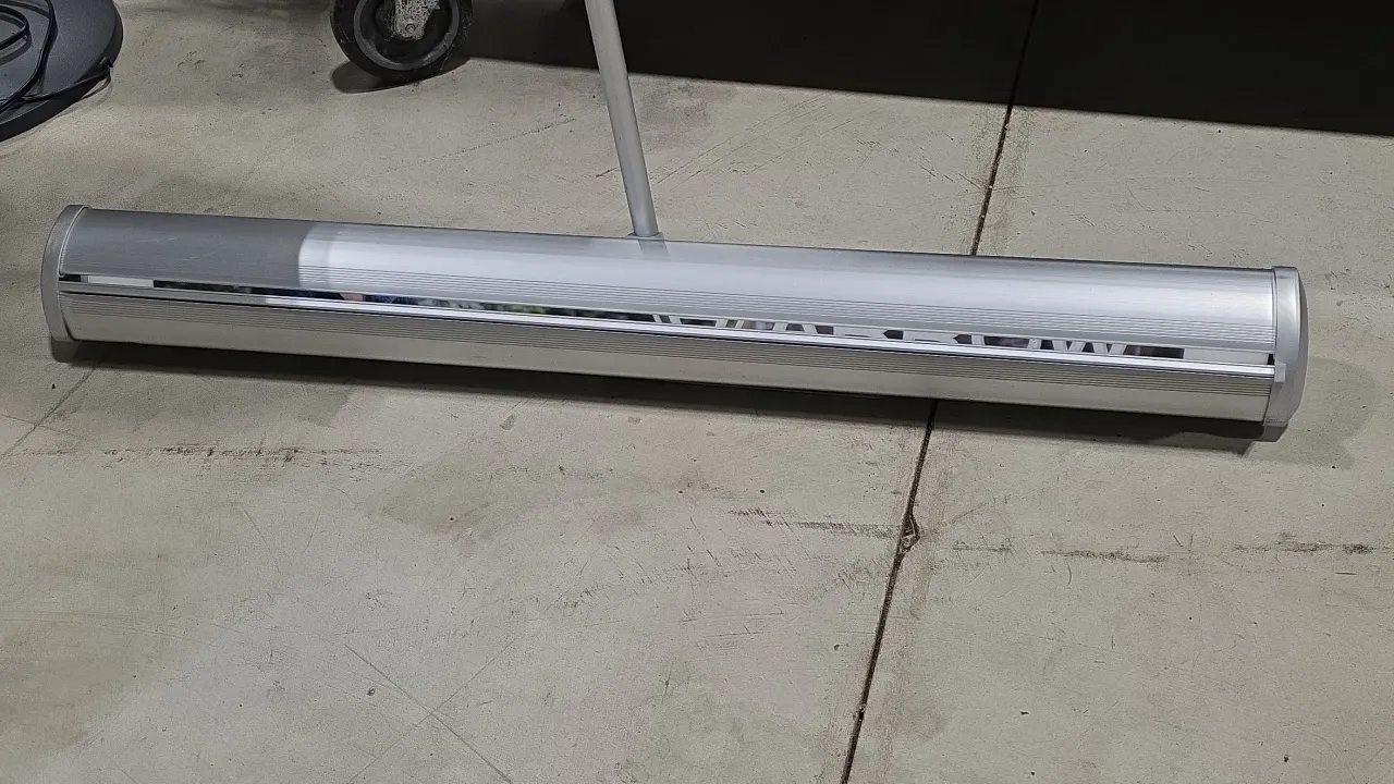 Aluminum roll-up retractable banner stand. Features silver-tone aluminum casing with collapsible support pole. 33.5" x 83".