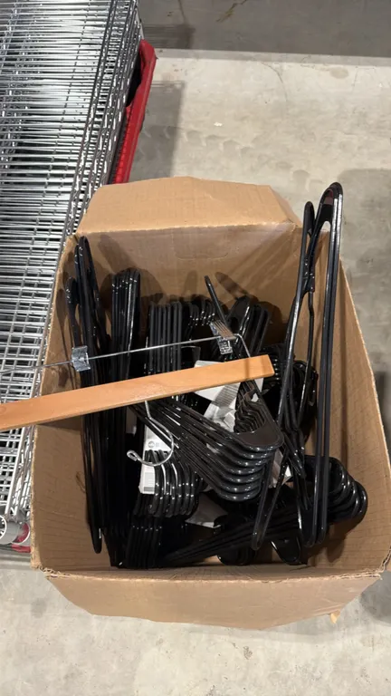 Box of assorted clothes hangers. Includes black plastic hangers and wooden pants clamp hanger.