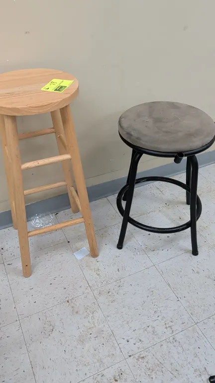 Pair of assorted stools. Includes (1) 30"H natural wood stool with round seat and rung footrests, and (1) black metal frame stool with round padded se