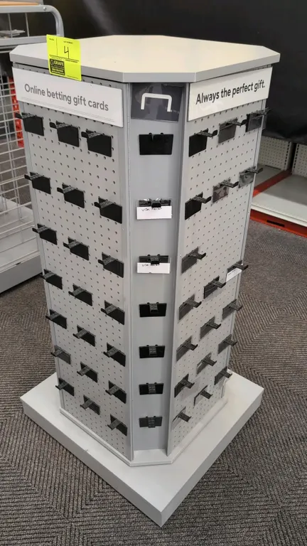 Laminate rotating merchandise display rack. Features multi-sided pegboard panels with plastic display hooks, corner card slots, and upper signage chan