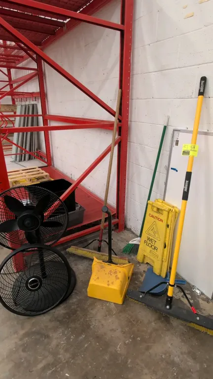 Assorted maintenance and cleaning supplies. Includes Lasko electric pedestal fan, push brooms, angle broom, upright lobby dustpan, hand dustpan, and f