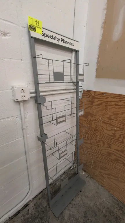 Metal multi-tier display rack. Features wire pockets with label holders, 'Specialty Planners' top header, and a freestanding base. Dimensions: 21"W x