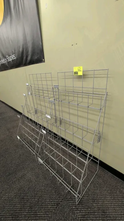 Metal wire merchandise display racks. Features multi-tier wire shelving with integrated price tag channels. Freestanding sloped wire frame design. 23"